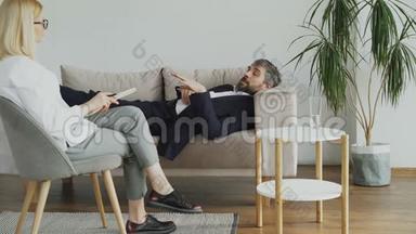 躺在沙发上的男人在办公室里和专业的心理治疗师或心理学家谈论他的问题